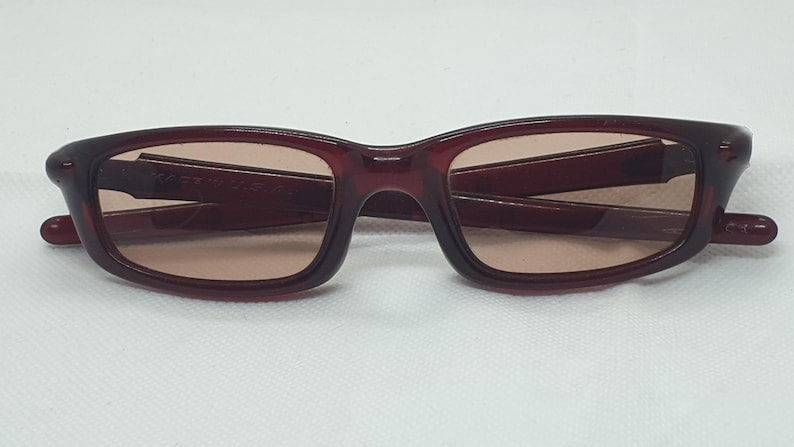 May include: Burgundy sunglasses with rectangular frames and tinted lenses. The glasses have a classic design. The arms of the glasses are folded. Suitable for everyday wear.