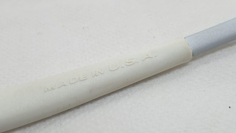 K&ouml;nnte beinhalten: Nahaufnahme eines wei&szlig;en Objekts mit dem gepr&auml;gten Text "MADE IN U.S.A.". Das Objekt hat eine zylindrische Form mit einem silberfarbenen Ende. Der Hintergrund ist eine schlichte wei&szlig;e Oberfl&auml;che.