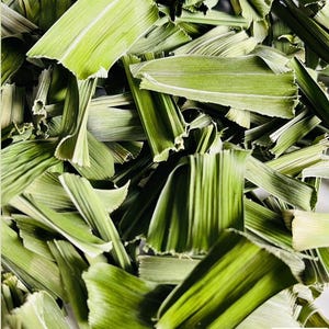 Op de afbeelding: Close-up van gedroogde citroengrasbladeren, met een levendige groene tint met lichtere, gedroogde randen. De bladeren zijn gelaagd, waardoor een textuur ontstaat. De afbeelding is goed belicht en benadrukt de natuurlijke details van het kruid.