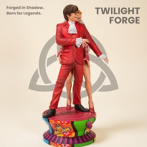 Pode incluir: Estatueta vermelha de um homem de fato vermelho e uma mulher de vestido vermelho, em pé sobre uma base colorida. A estatueta tem o texto "Twilight Forge" e "Oh Behave". A estatueta tem aproximadamente 25 cm de altura.