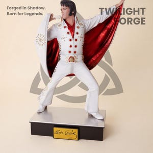 Può includere: Una statua bianca di Elvis Presley in posa da performance, che indossa una tuta bianca con abbellimenti dorati e un mantello rosso. La statua è su una base nera con una targhetta dorata. Il testo "Forged in Shadow. Born for Legends." è visibile.