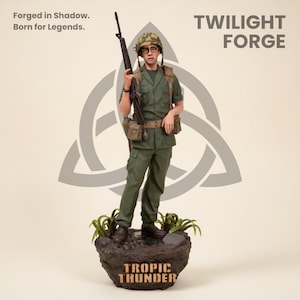 May include: A figurine of a soldier in a green uniform, holding a rifle, and wearing a helmet and glasses. The figurine stands on a rock base with the words "Tropic Thunder" and the Twilight Forge logo. The background includes the text "Forged in Shadow. Born for Legends."