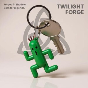 K&ouml;nnte beinhalten: Ein gr&uuml;ner, kaktusf&ouml;rmiger Schl&uuml;sselanh&auml;nger mit einem silbernen Schl&uuml;ssel und Ring. Der Schl&uuml;sselanh&auml;nger hat einen &uuml;berraschten Gesichtsausdruck und rennt. Der Text "Forged in Shadow. Born for Legends." und "TWILIGHT FORGE" sind sichtbar.