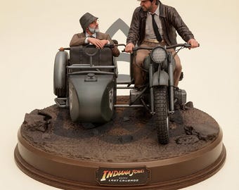 May include: A detailed collectible figurine featuring two figures on a dark green motorcycle with a sidecar. One figure wears a brown leather jacket and fedora, while the other wears a grey hat and suit. The base displays the text Indiana Jones Last Crusade.