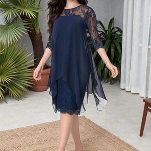 Puede incluir: Un vestido azul marino con corpi&ntilde;o y mangas de encaje. El vestido presenta un dise&ntilde;o en capas con una superposici&oacute;n fluida y transparente. El vestido llega a la rodilla y es adecuado para ocasiones formales.