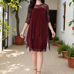 Puede incluir: Vestido burdeos con dise&ntilde;o en capas. El vestido presenta un corpi&ntilde;o y mangas de encaje, con una superposici&oacute;n transparente. El vestido llega a la rodilla y es adecuado para ocasiones formales.