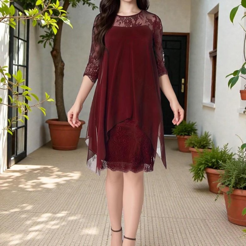 Puede incluir: Vestido burdeos con dise&ntilde;o en capas. El vestido presenta un corpi&ntilde;o y mangas de encaje, con una superposici&oacute;n transparente. El vestido llega a la rodilla y es adecuado para ocasiones formales.