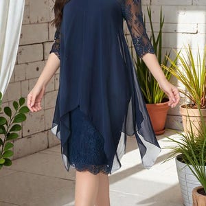 Puede incluir: Un vestido azul marino con corpi&ntilde;o y mangas de encaje. El vestido presenta un dise&ntilde;o en capas con una superposici&oacute;n transparente y fluida. El dobladillo est&aacute; adornado con encaje y el vestido tiene un escote redondo. El vestido es hasta la rodilla.