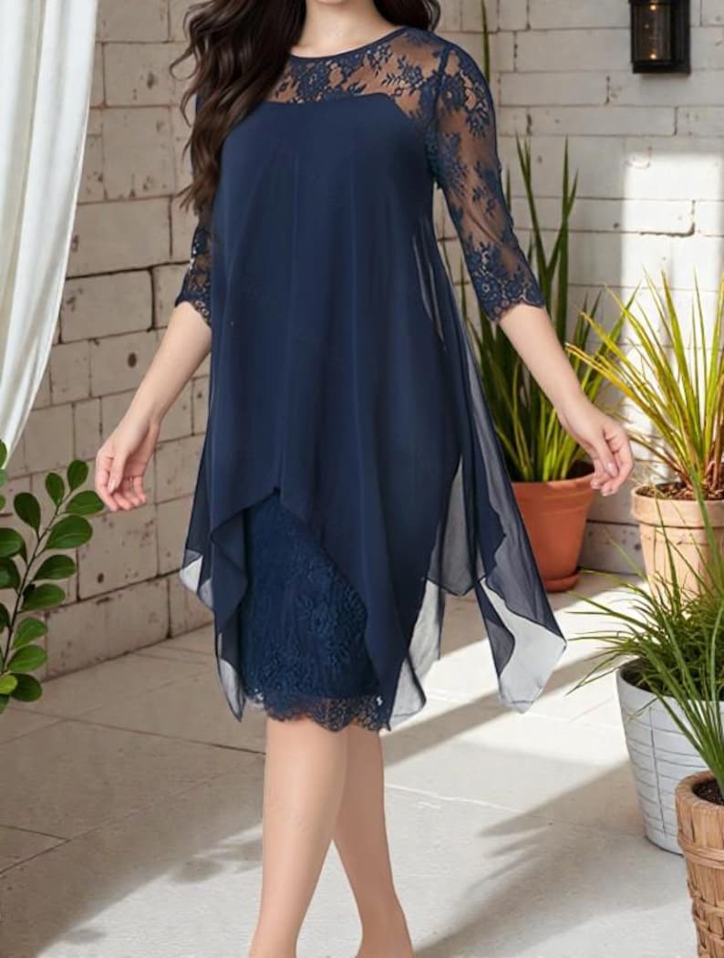 Puede incluir: Un vestido azul marino con corpi&ntilde;o y mangas de encaje. El vestido presenta un dise&ntilde;o en capas con una superposici&oacute;n transparente y fluida. El dobladillo est&aacute; adornado con encaje y el vestido tiene un escote redondo. El vestido es hasta la rodilla.