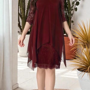 Puede incluir: Vestido burdeos con dise&ntilde;o en capas. El vestido presenta un corpi&ntilde;o y mangas de encaje, con una superposici&oacute;n transparente. El dobladillo es asim&eacute;trico y el vestido llega a la rodilla. El vestido se usa con tacones negros.