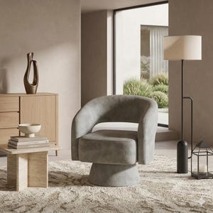 May include: A modern gray swivel armchair with a rounded back and armrests. The chair sits on a circular base and is placed on a patterned rug. A floor lamp with a beige shade and a decorative lantern are also visible.