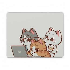 Pode incluir: Um tapete de rato retangular com fundo cinzento claro apresentando uma ilustração de desenho animado de três gatos. Um gato cinzento usa óculos, um gato malhado laranja digita num portátil e um gato branco segura uma caneca com a palavra CAT.