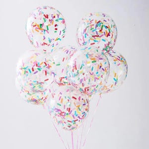 May include: A cluster of clear, round balloons filled with colorful confetti. The confetti pieces are in various colors, including red, yellow, green, and blue. The balloons are tied together with pink ribbons, creating a festive and celebratory look.