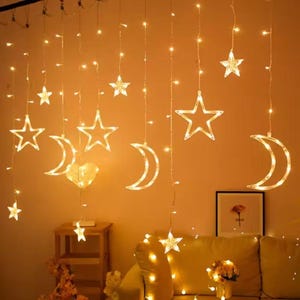 Könnte beinhalten: Warmweiße Lichterkette mit Stern- und Halbmondformen. Die Lichter hängen von der Decke und schaffen eine gemütliche und dekorative Atmosphäre. Ideal für ein Schlaf- oder Wohnzimmer.