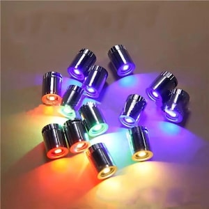 May include: A collection of small, cylindrical, metallic lights emitting various colors. The lights are arranged in a scattered pattern, with each light showcasing a different hue, including red, green, blue, and yellow.