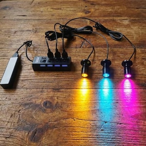 以下が含まれることがあります： 黄色、青、ピンクの光を発する3つの小さなスポットライトを備えた黒いUSBハブ。 スポットライトは黒いワイヤーでハブに接続されています。 白とグレーのモバイルバッテリーがハブに接続されています。