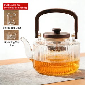 May include: A clear glass teapot with a wooden handle and lid. The teapot has a ribbed design and is filled with a golden liquid. The image also shows two clear tea liners and the text "Dual Liners for Steaming and Boiling".