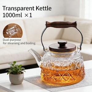 May include: A clear glass kettle with a wooden handle and lid, holding a golden liquid. The kettle has a capacity of 1000ml and is designed for both steaming and boiling. The text "Transparent Kettle 1000ml x 1" is visible.
