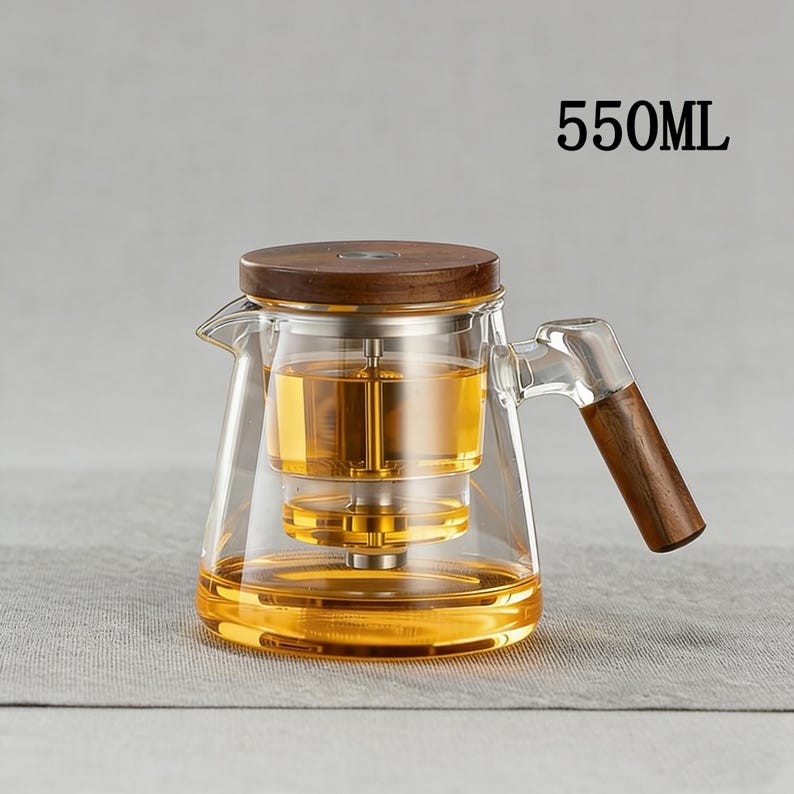 Pode incluir: Bule de vidro transparente com tampa e al&ccedil;a de madeira, cheio de l&iacute;quido &acirc;mbar. O bule tem um infusor embutido e o texto "550ML" &eacute; vis&iacute;vel. A al&ccedil;a e a tampa s&atilde;o feitas de madeira escura.