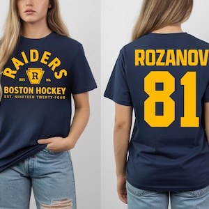 May include: Navy blue t-shirt with "RAIDERS BOSTON HOCKEY" text in yellow. The front of the shirt has a crest with the letter "R". The back of the shirt has the name "ROZANOV" and the number "81" in yellow.