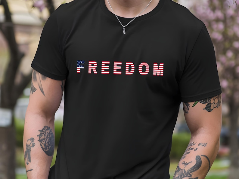 May include: Black t-shirt with the word "FREEDOM" printed across the chest in red, white, and blue. The letter "F" is designed with the American flag. The shirt is made of a soft material and is suitable for casual wear.
