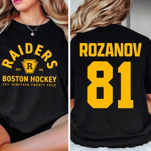May include: Black t-shirt with "RAIDERS" arched text in yellow, above a yellow and black crest with "R" inside. Below, "BOSTON HOCKEY" and "EST. NINETEEN TWENTY-FOUR" in yellow. The back features "ROZANOV" and the number "81" in yellow.