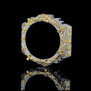 Könnte beinhalten: Ein silber- und goldfarbenes Armband mit einem sich wiederholenden Kreuzmuster. Das Armband hat eine strukturierte Oberfläche mit kleinen, funkelnden Details. Die Kreuze sind goldfarben und der Hintergrund ist silberfarben. Das Armband spiegelt sich in der schwarzen Oberfläche darunter.