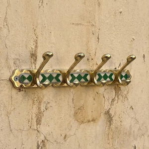 May include: A vintage brass wall-mounted coat rack with five hooks. The rack features a decorative design with green and white diamond-shaped accents. The hooks are curved and have a classic, elegant appearance.