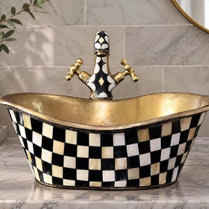 May include: An oval vessel sink featuring a black and white checkered pattern on the exterior and a metallic gold interior finish. A matching faucet with a black, white, and gold geometric design and two brass handles is mounted behind.