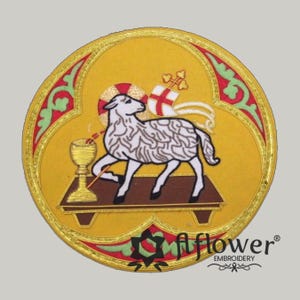 May include: A circular embroidered patch featuring a white lamb standing on a brown platform next to a gold chalice. The lamb has a red cross banner and a halo. The background is yellow with green and red decorative borders and gold thread.