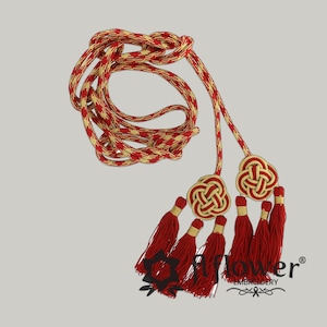Puede incluir: Cordón decorativo rojo y dorado con borlas. El cordón presenta un diseño trenzado de hilos rojos y dorados. Las borlas son rojas con detalles dorados, unidas a nudos decorativos. Probablemente utilizado con fines decorativos.