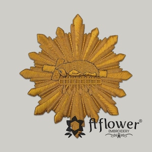 May include: Gold embroidered emblem featuring a central design of a reclining animal on a platform, surrounded by a sunburst pattern. The emblem is intricately detailed with a textured appearance, and the color is a rich gold.