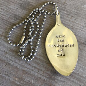 May include: A silver spoon necklace with a quote that reads "tame the savageness of man".
