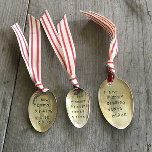 May include: Three silver spoons with red and white striped ribbon tied around the handle. Each spoon has a different saying engraved on it: "I saw mommy kissing Santa Claus", "I saw mommy kissing Santa Claus", and "I saw mommy kissing Santa Claus".
