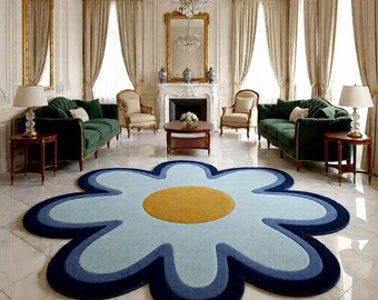 May include: A large, flower-shaped rug with a light blue, medium blue, and navy blue design, and a yellow center. The rug is in a living room with green sofas, gold-framed mirrors, and cream-colored curtains.
