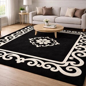 May include: A black area rug with a white floral design in the center and a white scrollwork border. The rug is rectangular and placed in a living room setting with a sofa, chairs, and a coffee table.