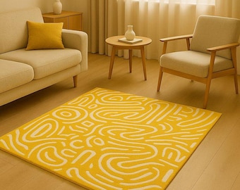 May include: A yellow rectangular rug with a white abstract design of curved lines and shapes. The rug is placed on a wooden floor in a living room setting, with a sofa, armchair, and side table visible.