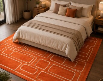 May include: An orange rectangular rug with a geometric white design is placed in a bedroom. The rug is under a bed with a beige headboard and bedding. Decorative pillows in shades of brown and orange are on the bed.