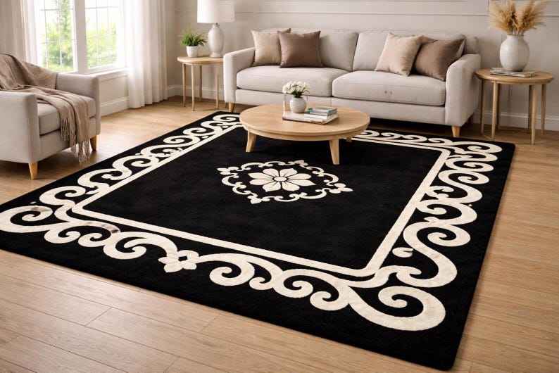 May include: A large, rectangular black area rug with a cream-colored border and central floral design. The border features a repeating scroll pattern. The rug is placed on a hardwood floor in a living room setting.