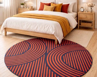 May include: A round rug with a navy blue background and a repeating pattern of orange curved lines. The rug is placed on a wooden floor in a bedroom setting, with a bed and nightstands visible in the background.