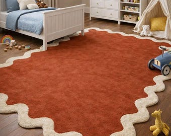 May include: A large, rust-colored rug with a cream-colored, wavy border. The rug is in a child's bedroom, with a white bed, dresser, and a play teepee. A blue toy car and a yellow giraffe toy are on the floor.