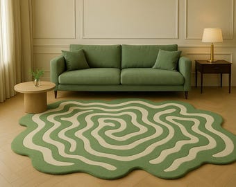 May include: A green sofa with two matching throw pillows sits against a wall. A round, light-colored side table holds a small vase. A large, green and cream-colored rug with a wavy design is on the floor.