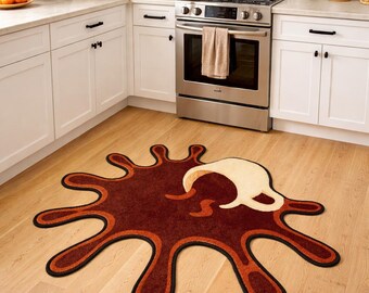 May include: A unique coffee-themed rug in a kitchen setting. The rug is shaped like a coffee spill, featuring shades of brown, orange, and black. A cream-colored coffee cup design is incorporated into the spill. The rug is placed on a light wood floor.
