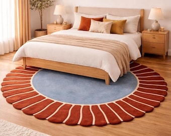 May include: A bedroom scene featuring a round rug with a rust-colored scalloped border and a light blue center. The rug is placed under a wooden bed frame with white bedding and decorative pillows. A small tree and lamps complete the decor.