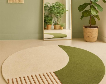 May include: A round rug with a cream-colored half and a green half, with brown stripes on the cream section. The rug is on a light-colored floor. A large mirror and a potted plant are in the background.
