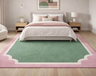 May include: A bedroom scene featuring a large green rug with a pink scalloped border. The rug is centered under a bed with white bedding and pink accents. Two wooden nightstands flank the bed.