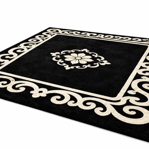 May include: A square black rug with a cream-colored floral design in the center and a cream-colored border with a scroll pattern. The rug is on a white background.