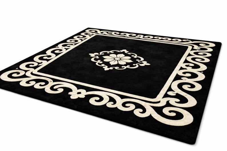 May include: A square black rug with a cream-colored floral design in the center and a cream-colored border with a scroll pattern. The rug is on a white background.