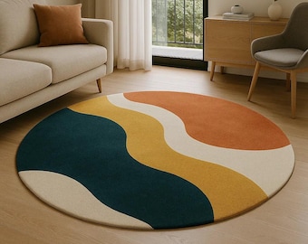 May include: A round area rug with an abstract design. The rug features flowing, wavy bands of color, including teal, yellow, orange, and cream. The rug is placed on a hardwood floor, and the overall aesthetic is modern and stylish.