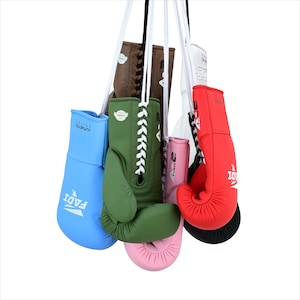 May include: A collection of boxing gloves in various colors, including blue, green, pink, red, brown, and white. The gloves are hanging from white cords against a white background. The gloves have laces and the brand name "FADI" is visible on some.